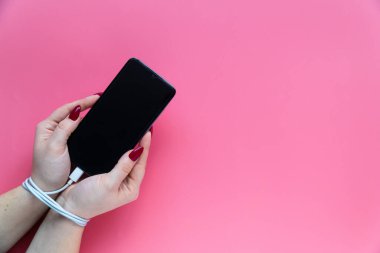 Kadın eli kapalı pembe arka planda modern bir akıllı telefon var. İnternet ve aygıtlara bağımlılıklar