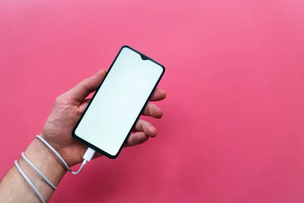 Yakın plan erkek eli pembe arka planda boş ekranı olan modern bir akıllı telefona sahip. Sosyal ağ sitelerine, internete ve aygıtlara bağımlılıklar .