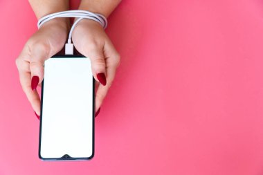 Modern akıllı telefona sahip bir kadının ellerini kapat. Metnin ya da tasarımın için boş bir ekran. Elleri telefon şarj aleti ya da bornozla bağlı. Sosyal ağ sitelerinde, internet ve aygıtlarda bağımlılıklar .