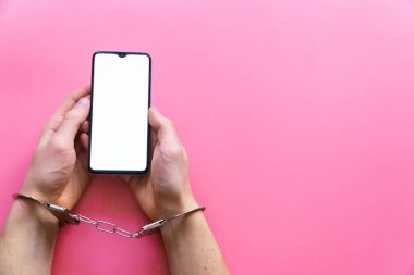 Elleri kelepçeli erkekler pembe arka planda akıllı telefon tutarlar. İnternet ve aygıt bağımlılığı kavramı.