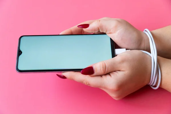 Yan görünüşlü kadın elleri modern akıllı telefona sahiptir, mesaj veya logo için boş ekran. Elleri telefon şarj aleti ya da bornozla bağlı. Sosyal ağ sitelerine, internete ve aygıtlara bağımlılık .