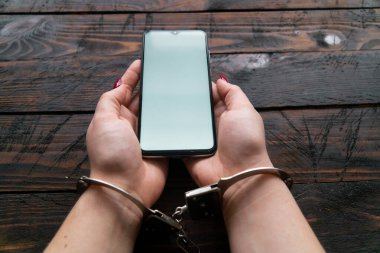 Kelepçeli üst görüşlü kadın ahşap arka planda modern bir akıllı telefon tutuyor. İnternet ve cihaz ekleme kavramı