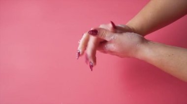 Yavaş çekim yapan kadın ellerini pembe arka planda köpürüyor.