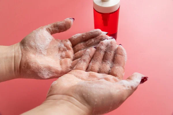 Kadın pembe arka planda sıvı sabunla ellerini sabunluyor.