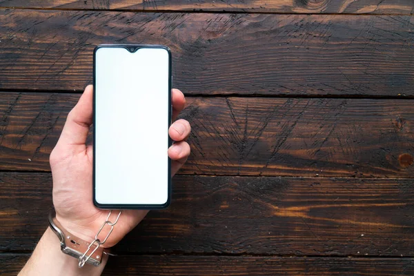 Elleri kelepçeli adamlar mesaj ya da logo için boş ekranı olan modern bir akıllı telefon tutuyorlar. İnternet bağımlılığı, sosyal ağ ve aygıtlar kavramı.
