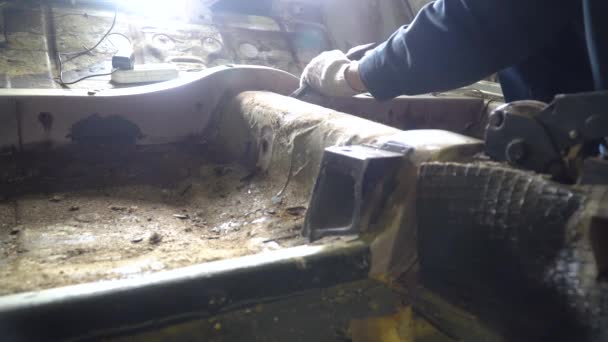 Travailleur frappe les vieux mastics au fond de la voiture avec un ciseau et un marteau 