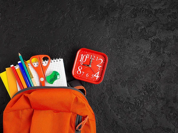 Orange backpack with school supplies on a black concrete background. The concept of the school. Copy space.