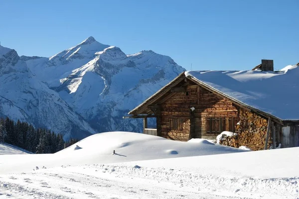 Facade of a old timber hut and snow covered mount Oldenhorn. Win — Stock Photo, Image