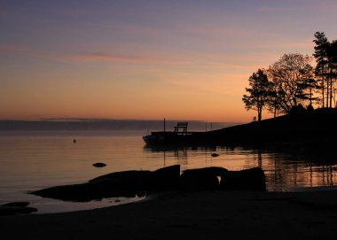 Parlak turuncu sabah gökyüzü ve Vanern Gölü kıyısı, İsveç.