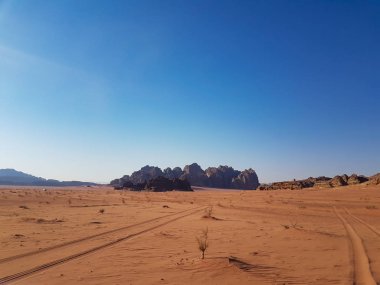 Kuru bir arazinin manzarası ve çöldeki kum. Ürdün 'deki Wadi Rum çölünde kum tepeleri ve lastik izleri. Çölde mavi gökyüzü ile aydınlık güneşli bir gün.