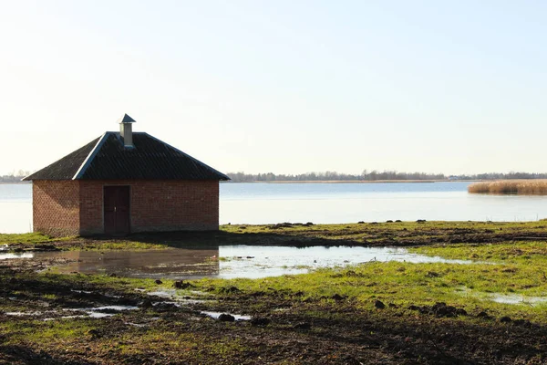 Flooded brick house that stand at the lake coast. Boat house build of red bricks that stand on a flooded green loan.
