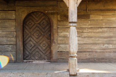 Ahşap ahşap evin önünde kapısı oyulmuş bir eşik. Terasta kavis ve oyma sütun. 