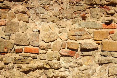 Taştan yapılmış eski bir duvar. Ortaçağ kayalık yüzeyi. Çimentoyla tutturulmuş eski bir kayanın dokusu. Ortaçağ duvarında güneş küçük gölgeler oluşturur. 