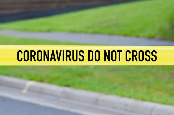 Coronavirus do not cross yellow warning tape with street and green yard in background