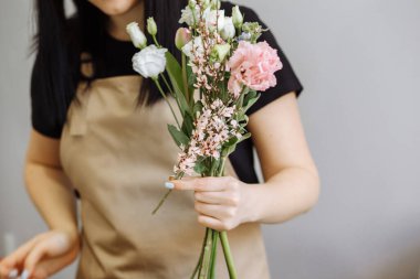 Kum önlüklü çiçekçi kız östomalı bir buket hazırlıyor.