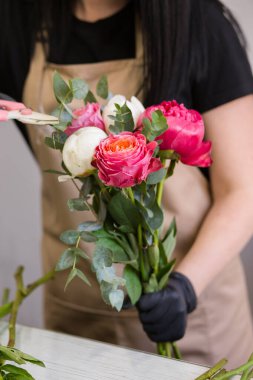 Siyah eldivenli çiçekçi bir buket kırmızı şakayık yapıyor.