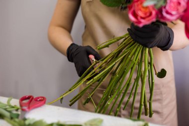 Siyah eldivenli çiçekçi bir buket kırmızı şakayık yapıyor.