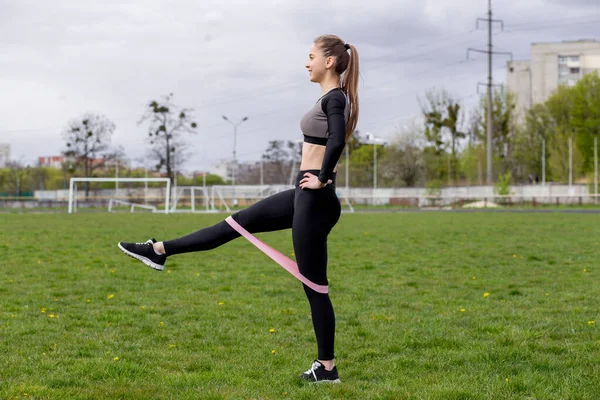 Spor salonundaki kız spor yapıyor. Yeşil bir çimenlikte diş etleriyle egzersiz yapıyor ve güç egzersizleri yapıyor.
