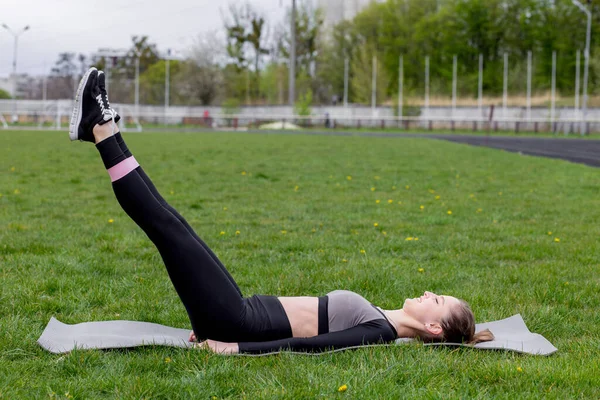 Spor salonundaki kız spor yapıyor. Yeşil bir çimenlikte diş etleriyle egzersiz yapıyor ve güç egzersizleri yapıyor.