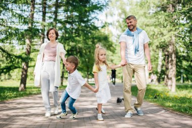 Parkta yürüyen iki çocuklu mutlu bir aile..