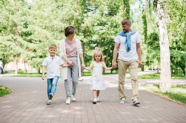 Parkta yürüyen iki çocuklu mutlu bir aile..
