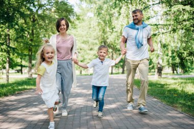 Parkta yürüyen iki çocuklu mutlu bir aile..