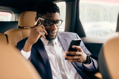 Takım elbiseli bir işadamı arabada oturur ve akıllı telefonunu kullanır..