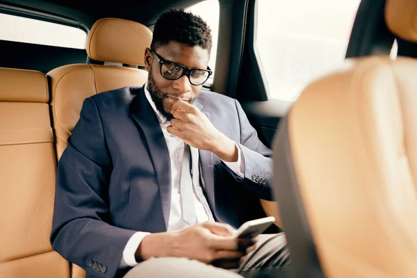 Egy öltönyös üzletember ül a hátsó ülésen a telefonjával.. — Stock Fotó