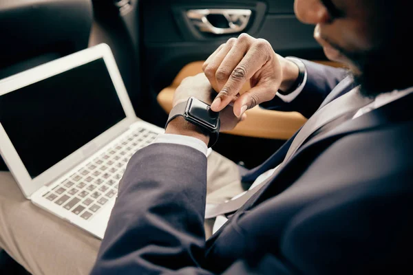Nahaufnahme eines Mannes, der mit einem Laptop im Hintergrund Uhren im Auto betrachtet. — Stockbild Nahaufnahme eines Mannes, der Uhren im Auto betrachtet. — Stockfoto
