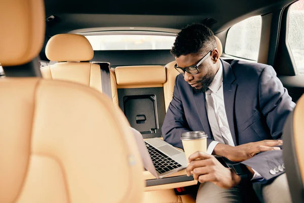 Uomo seduto sul sedile posteriore con il suo caffè e lavorare sul computer portatile . — Foto Stock