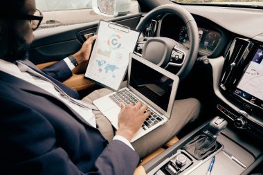 Businessman working on the laptop and looking at the notepad.