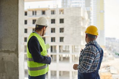 İki mühendis, katlanmış planı tutan birlikte iş ilgili soruları tartışmak.