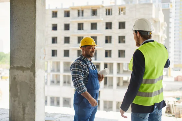 Dos ingenieros discuten preguntas relacionadas con el trabajo juntos manteniendo un plano plegado . — Foto de Stock