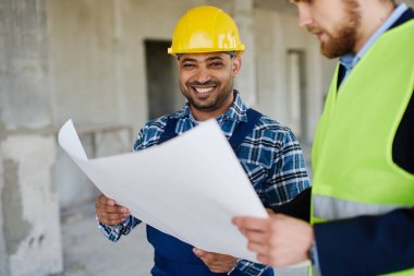 İki mühendis ellerinde tuttukları taslakları tartışıyor ve kameraya gülümsüyor..