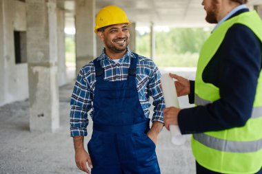 İki mühendis, katlanmış planı tutan birlikte iş ilgili soruları tartışmak.