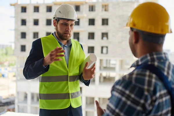 Dos ingenieros discuten preguntas relacionadas con el trabajo juntos manteniendo un plano plegado . — Foto de Stock