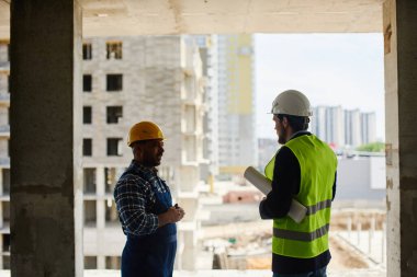 Miğferli bir mühendis telefonla konuşuyor ve yakın planda bir not defteri tutuyor..