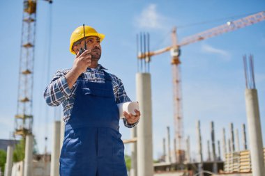 Bir mühendis, iş yerinde katlanmış bir taslak ile radyo kullanıyor..