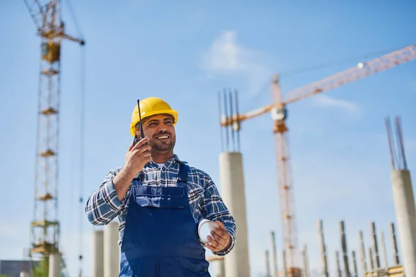 Ein Ingenieur benutzt ein Funkgerät an seinem Arbeitsplatz mit gefaltetem Entwurf. — Stockfoto