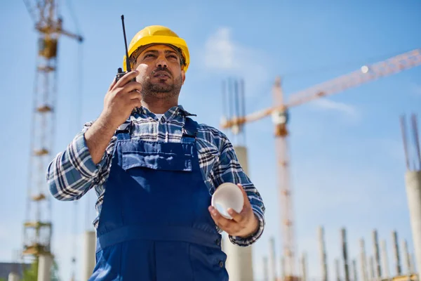 An engineer uses radio set on his work place with a folded draft.