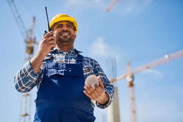 An engineer uses radio set on his work place with a folded draft.