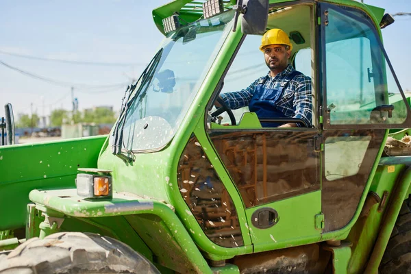 Un ingegnere in uniforme guida un trattore verde . Immagini Stock Royalty Free