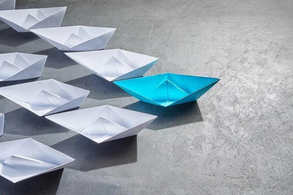 Business Concept, Paper Boat, η βασική γνώμη Leader, η έννοια της επιρροής. Ένα μπλε χάρτινο σκάφος ως ηγέτης, που οδηγεί προς την κατεύθυνση των λευκών πλοίων σε ένα γκρίζο φόντο από τσιμέντο, αντίγραφο χώρου — Φωτογραφία Αρχείου