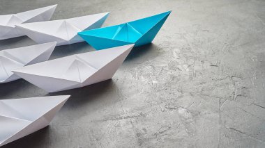 İş liderliği kavramı, Paper Boat, anahtar fikir lideri, nüfuz kavramı. Lider olarak mavi kağıttan bir tekne, gri beton arka planda beyaz gemilere doğru gidiyor.,