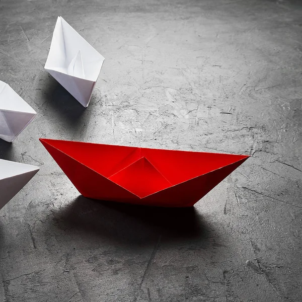 İş liderliği kavramı, Paper Boat, anahtar fikir lideri, nüfuz kavramı. Lider olarak bir kırmızı kağıt tekne, gri beton arka planda beyaz gemilere doğru gidiyor.