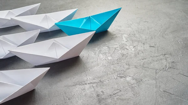 Business leadership Concept, Paper Boat, the key opinion Leader, the concept of influence. One blue paper boat as the Leader, leading in the direction of the white ships on a gray concrete background,