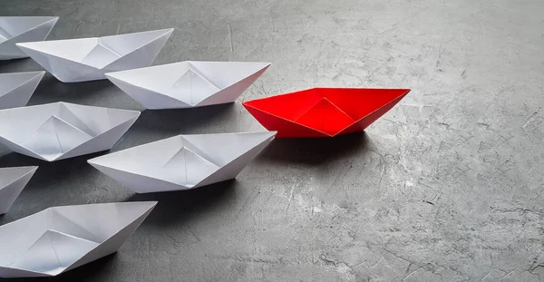 İş liderliği kavramı, Paper Boat, anahtar fikir lideri, nüfuz kavramı. Lider olarak bir kırmızı kağıt tekne, gri beton arka planda beyaz gemilere doğru gidiyor. — Stok fotoğraf