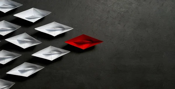 Business leadership Concept,key opinion Leader, the concept of influence. One red paper boat as the Leader, leading in the direction of the white ships on a gray concrete background,copy space,flat la