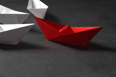 İş liderliği kavramı, Paper Boat, anahtar fikir lideri, nüfuz kavramı. Lider olarak bir kırmızı kağıt tekne, gri beton arka planda beyaz gemilere doğru gidiyor.