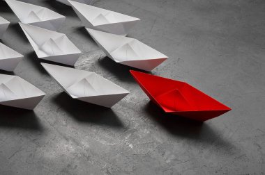 İş liderliği kavramı, Paper Boat, anahtar fikir lideri, nüfuz kavramı. Lider olarak bir kırmızı kağıt tekne, gri beton arka planda beyaz gemilere doğru gidiyor.